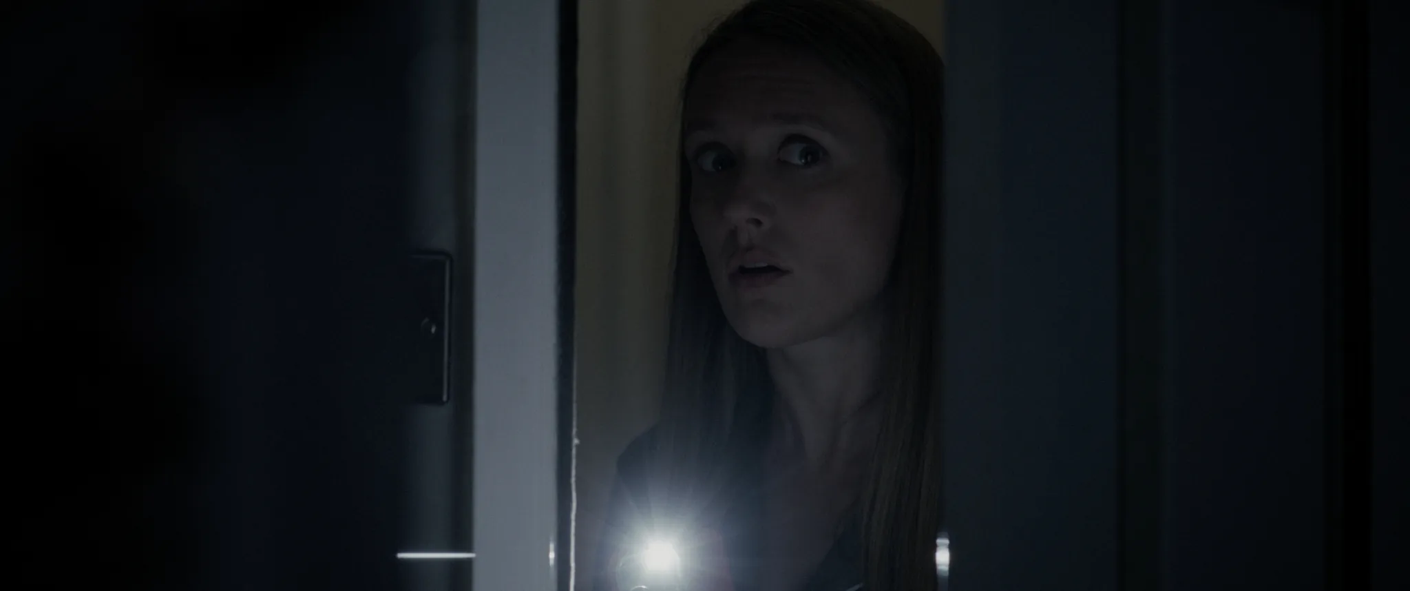 A face in the doorway, lit by a phone torch